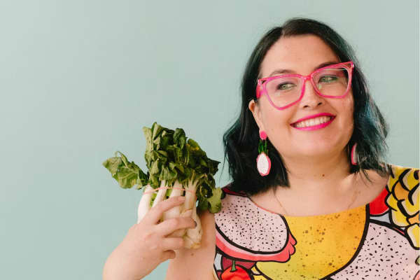 A smilin gwoman in pink glasses holds a bunch of bok choy.