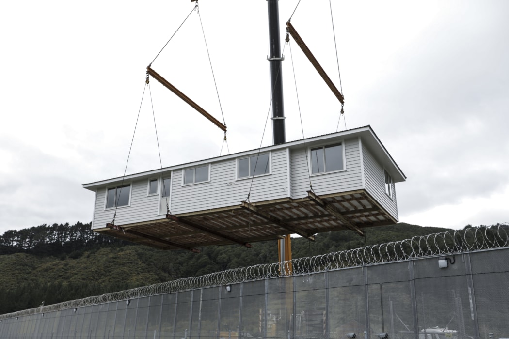 The first house being built by carpentry students at the prison has been completed, a crane lifted the building over the wire so it can be transferred to a permanent site.