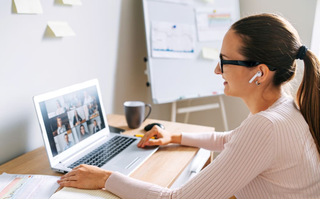 Morning meeting online. A young woman is using app on laptop for connection with colleagues, employees. Video call with many people together. Back view