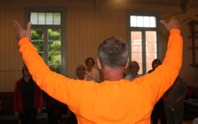 A photo of choirmaster Bert van Dijk conducting the Devonport World Song Choir.