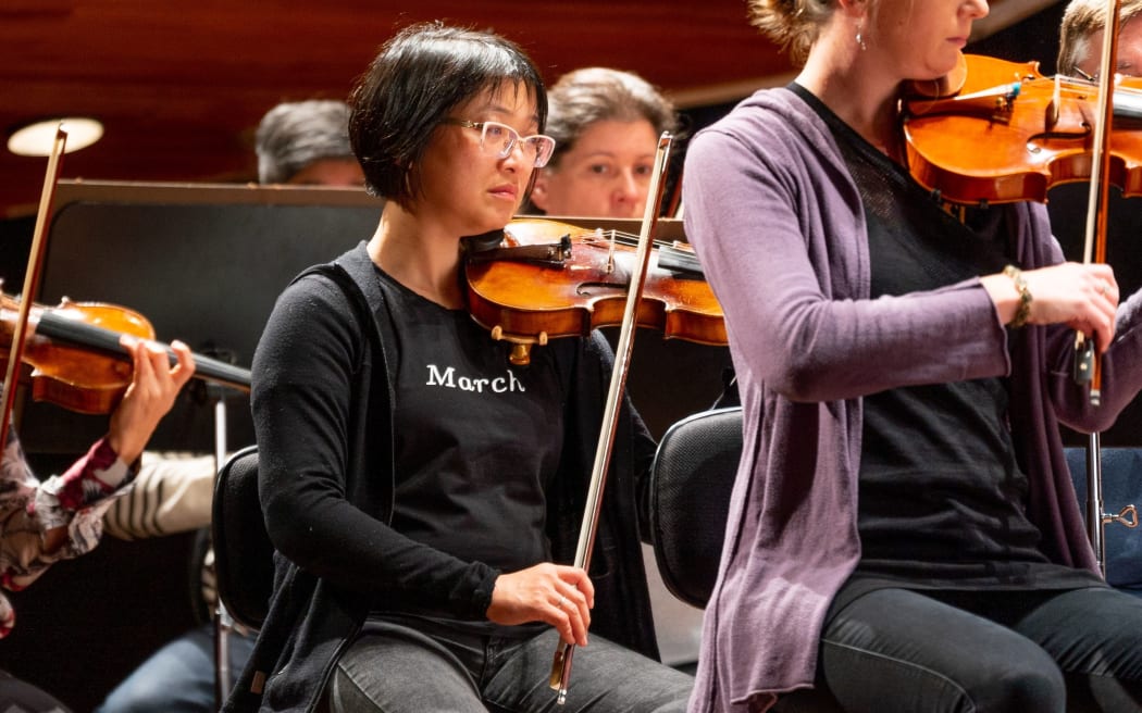 NZSO first violinist Haihong Liu playing her instrument with other musicians around her.