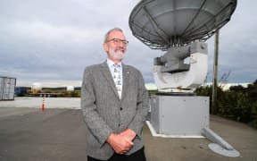 A man wearing a jacket and tie and glasses  stands in front of a satellite dis