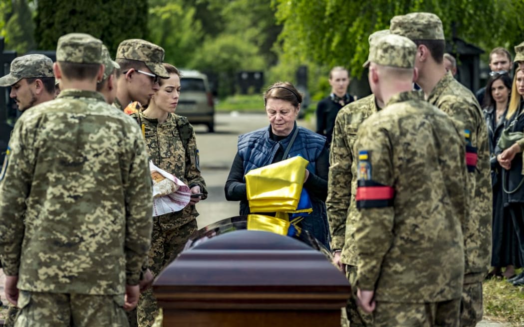The mother of Ukrainian soldier Eugene Kvaskov receives a flag from soldiers during his funeral in Kyiv, in May 2023.