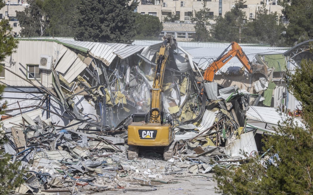 A photograph shows machinery demolishing a structure inside the headquarters of the United Nations Relief and Works Agency (UNRWA) in the Sheikh Jarrah neighbourhood of Israeli-annexed east Jerusalem on January 20, 2026. Israeli bulldozers began demolitions at the headquarters of the UN agency for Palestinian refugees in east Jerusalem on January 20, in what the organisation called an "unprecedented attack". The compound in Israeli-annexed east Jerusalem has been empty of UNRWA staff since January 2025, when a law banning its operations took effect after a months-long battle over its work in the Gaza Strip. (Photo by ILIA YEFIMOVICH / AFP)