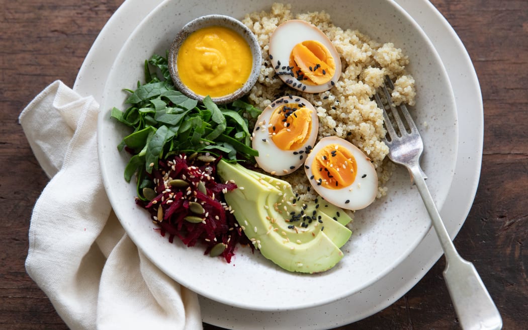 A bowl containing avocado, soy marinated eggs, greens and a carrot miso dressing.