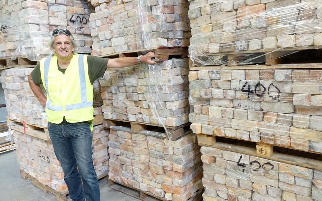 Man stands by pallets of plastic wrapped bricks.