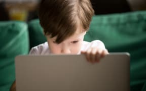 A photo of a Curious interested kid boy secretly looking watching forbidden censored adult only internet online video content on laptop alone, parental protection, computer control and security for child concept