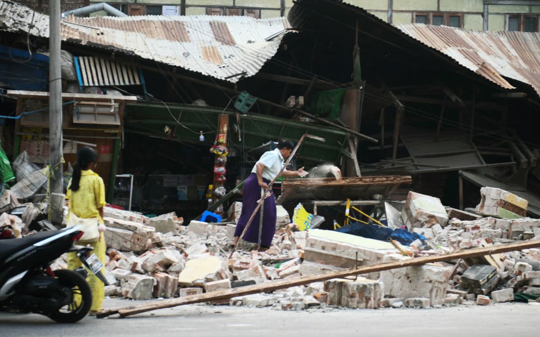 A woman clears debris in front of damaged houses in Mandalay on March 30, 2025, two days after an earthquake struck central Myanmar. The death toll from a huge earthquake that hit Myanmar and Thailand passed 1,600, as rescuers dig through the rubble of collapsed buildings in a desperate search for survivors. The quake destroyed buildings, downed bridges and buckled roads across swathes of Myanmar, with massive destruction seen in Mandalay. (Photo by Sai Aung MAIN / AFP)