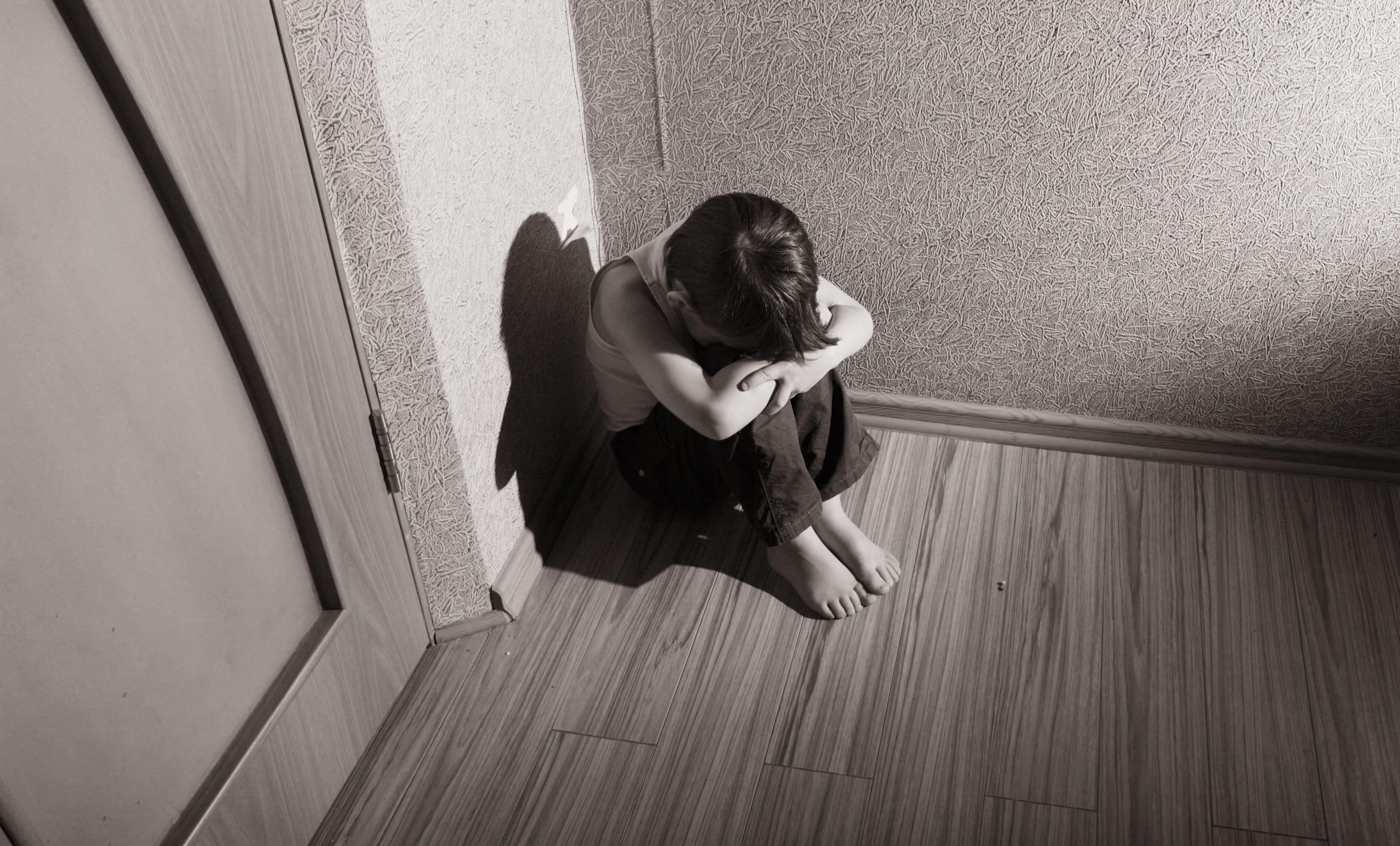 A young boy sits in the corner with his head in his hands (file photo)