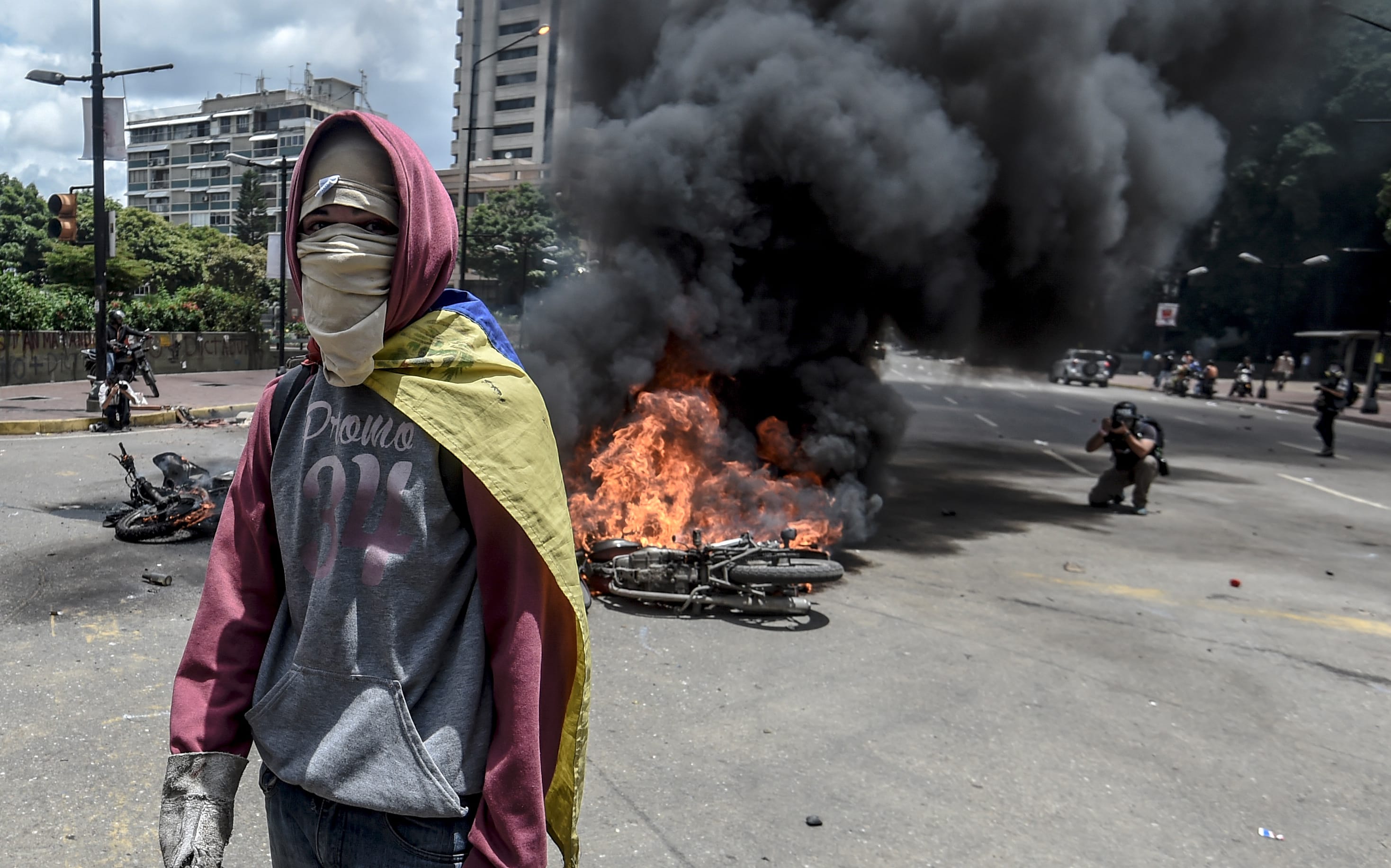 An anti-government activist stands in front of burning police bikes during a protest in Caraca against the elections for a Constituent Assembly.