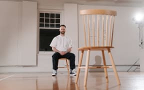 Artist Hamish Annan sits in a wooden chair across form a empty wooden chair as part of his performance Access.