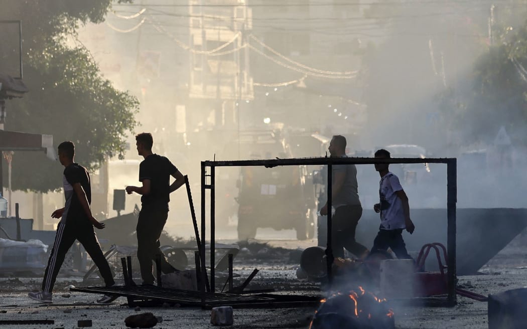 Palestinians walk past burned waste during an Israeli military operation in the Jenin refugee camp in the occupied West Bank on July 3, 2023. Israel has stepped up operations in the northern West Bank, home to Jenin city and its adjacent refugee camp, a stronghold of Palestinian armed groups where there has been a spate of attacks on Israelis as well as attacks by Jewish settlers on Palestinian communities. (Photo by Jaafar ASHTIYEH / AFP)