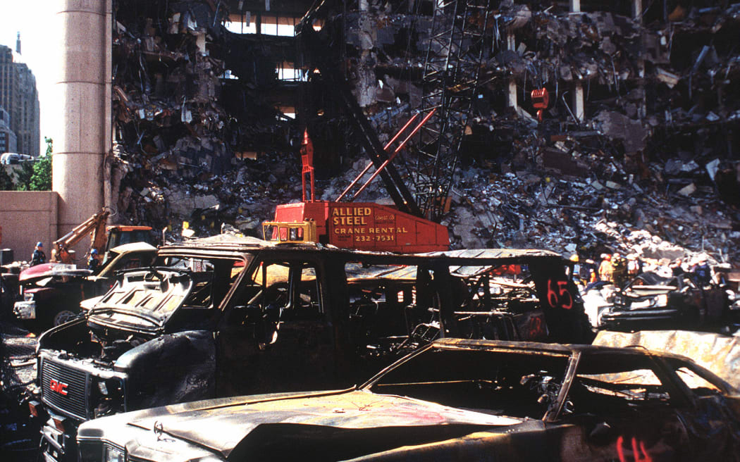 The bombed remains of automobiles with the bombed Federal Building in the background.  The military is providing around the clock support since a car bomb exploded inside the building on Wednesday, April 19, 1995.