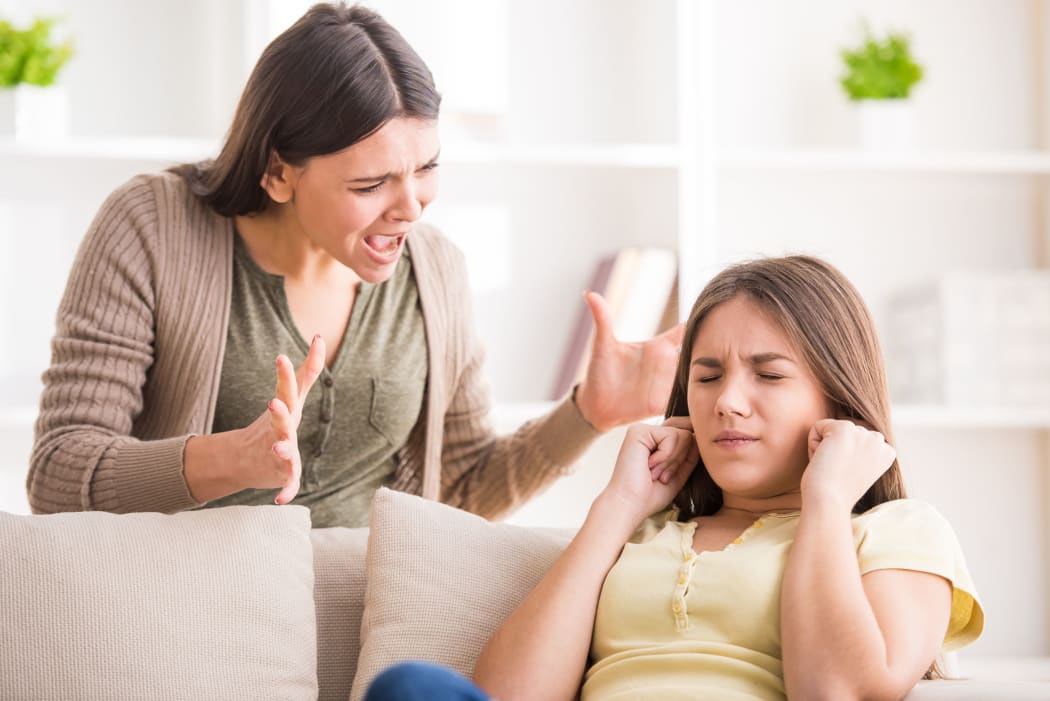 A photo of a mother shouting at her daughter. The girl is closing her eyes and has her hands over her ears.
