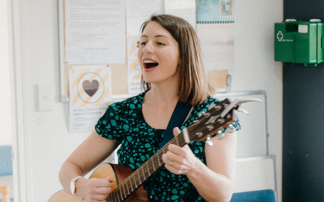 Rachel Foxell plays guitar in what looks like a waiting room.