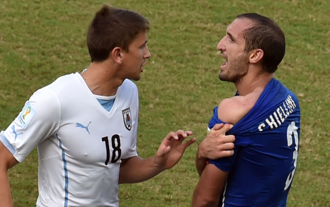 Italy's defender Giorgio Chiellini shows an apparent bitemark by Uruguay forward Luis Suarez to Uruguay's midfielder Gaston Ramirez during a  match between Italy and Uruguay during the World Cup.