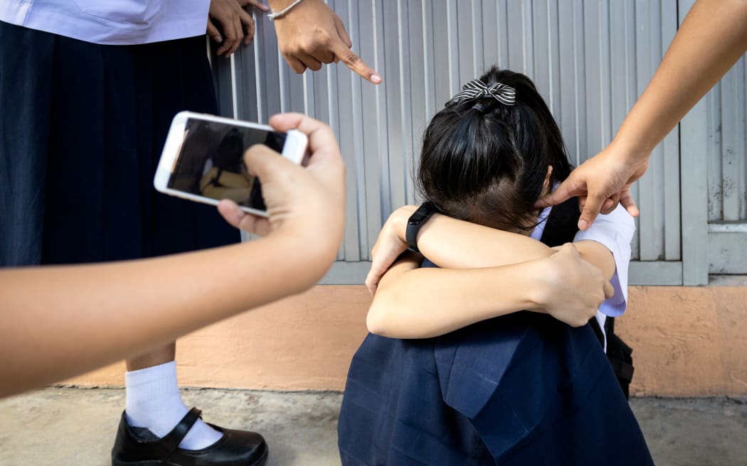 Problem of bullying at school,sad stressed asian girl student in Thai school uniform sitting on the floor with hands on knees,scared,anxious victim of bullying and video recorded on a mobile phone