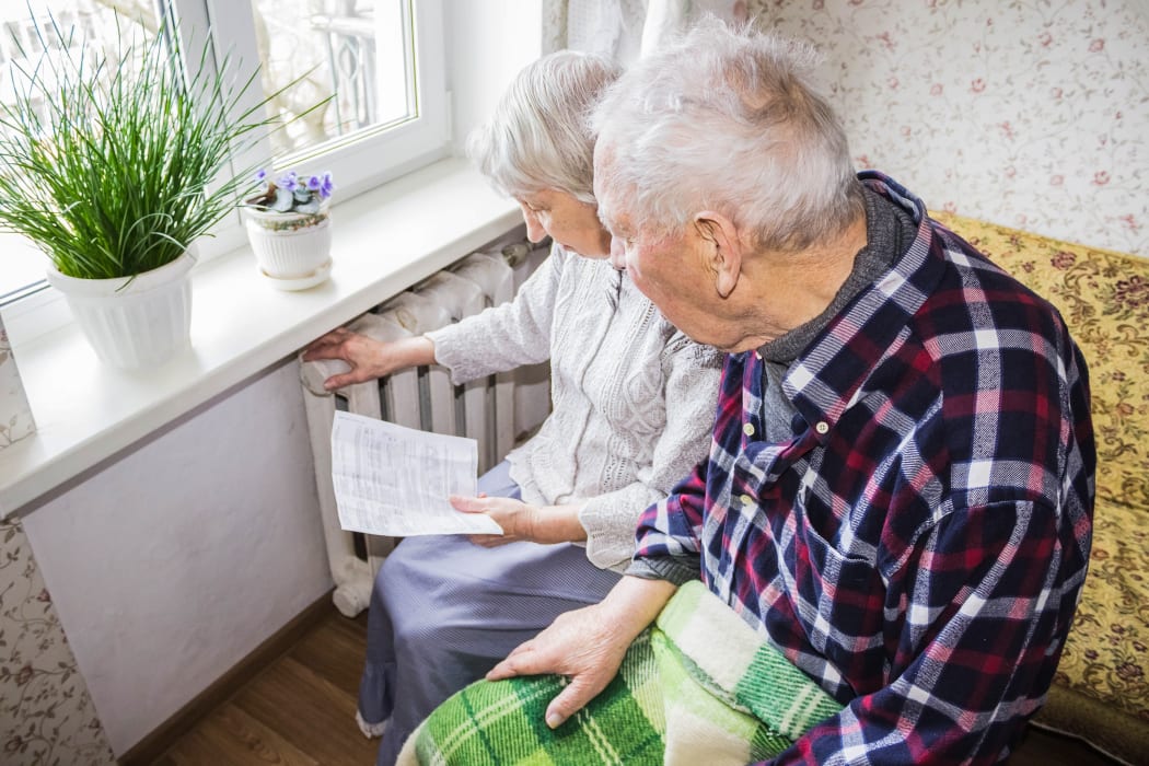 The senior woman holding gas bill in front of heating radiator. Payment for heating in winter.