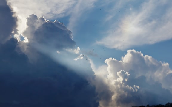 Dark and white clouds with shafts of sunlight and patches of blue sky.