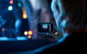 Woman use mobile phone shooting video photo of concert in front of stage at night with beautiful blurred bokeh from the lights in background