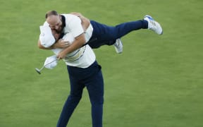 Shane Lowry lifts teammate Tyrrell Hatton after Hatton halved his match to win the Ryder Cup for Europe against the United States at Bethpage Black course in New York, September 28, 2025. (Photo by Harry How / GETTY IMAGES NORTH AMERICA / Getty Images via AFP)