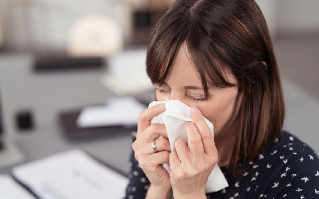 Close up Sick Young Office Lady at her Desk Sneezing Into a White Tissue with Eyes Closed.