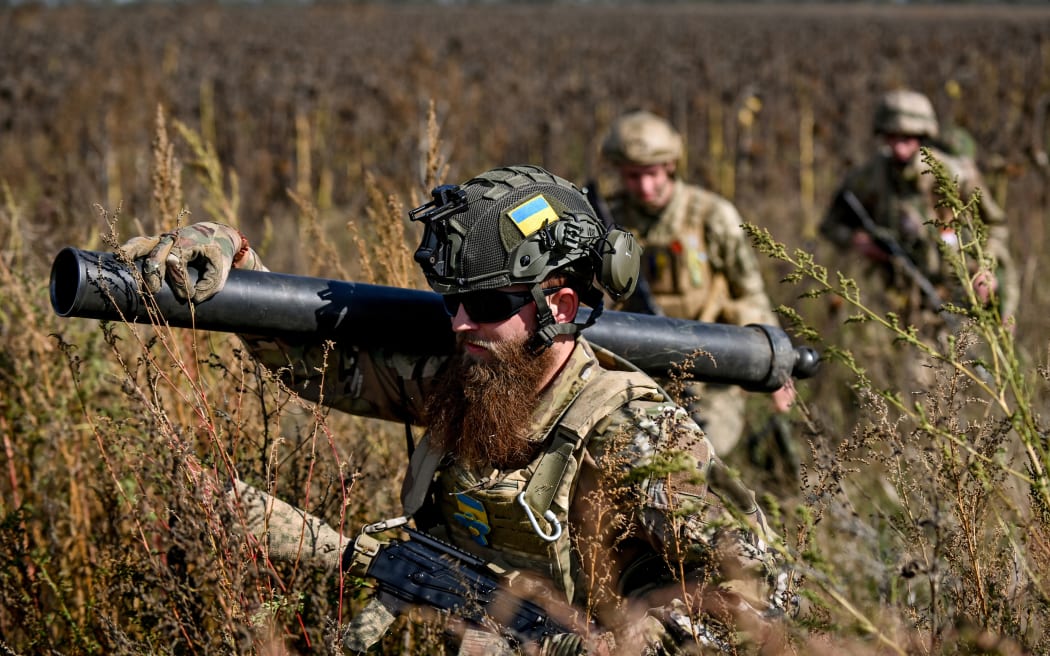 Military mortar crew march through a field of dry sunflowers, Zaporizhzhia Region, southeastern Ukraine.