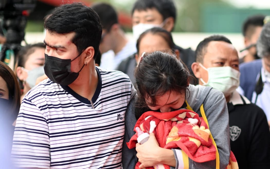 Sittipong Taothawong (L) comforts his wife Kanjana Buakumchan as she holds their child's milk bottle and blanket while standing outside the nursery in Na Klang in Thailand's northeastern Nong Bua Lam Phu province on October 7, 2022, the day after a mass shooting at the site.