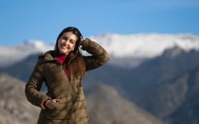 Happy tourist touching her hair while enjoying a beautiful snowy mountain view on a sunny winter day