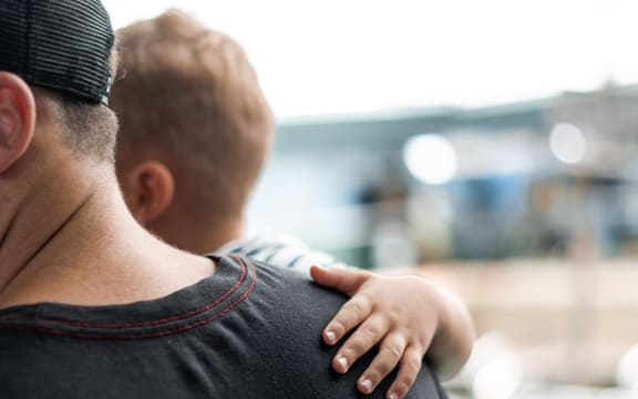 A person wearing a cap carries a child who has their arm wrapped around them.