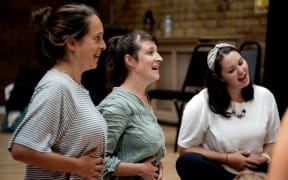 Three mums place their hands on their stomachs as they sing.