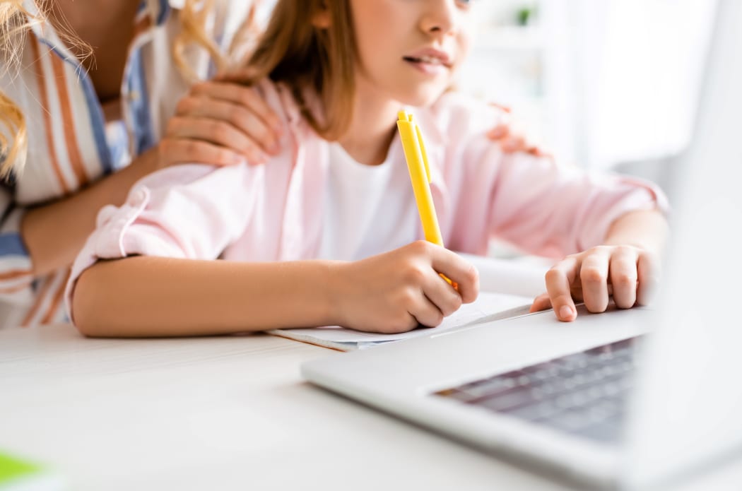 Cropped view of woman embracing kid writing on notebook near laptop on table