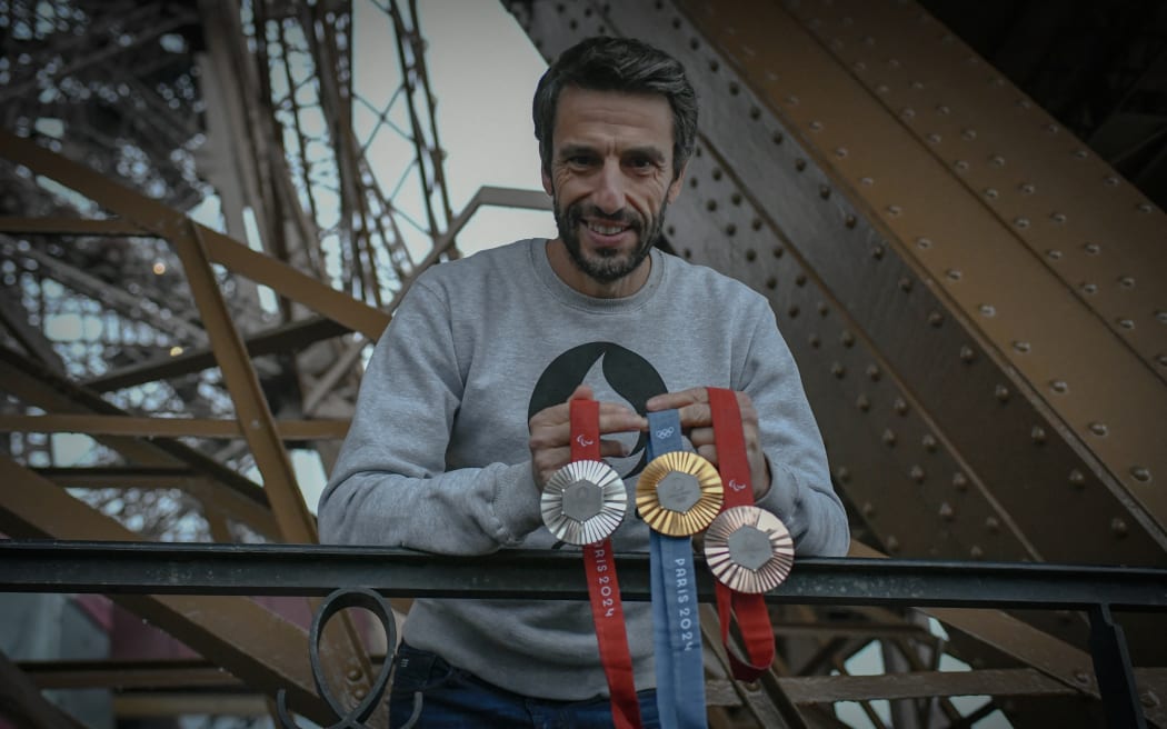 French President of the Paris Organising Committee of the 2024 Olympic and Paralympic Games Tony Estanguet poses with olympics 2024 medals on February 01, 2024 at the Eiffel tower in Paris. On the medals' head side, the engraved figures of the goddess of victory Athena, Nike, the Panathenaic stadium and the Acropolis are imposed by the International Olympic Committee (IOC) but Paris 2024 has obtained exceptional authorization to add the design of the Eiffel Tower, and use 18 grams of Eiffel Tower metal on each medal, extracted from pieces of the tower. (Photo by STEPHANE DE SAKUTIN / AFP)