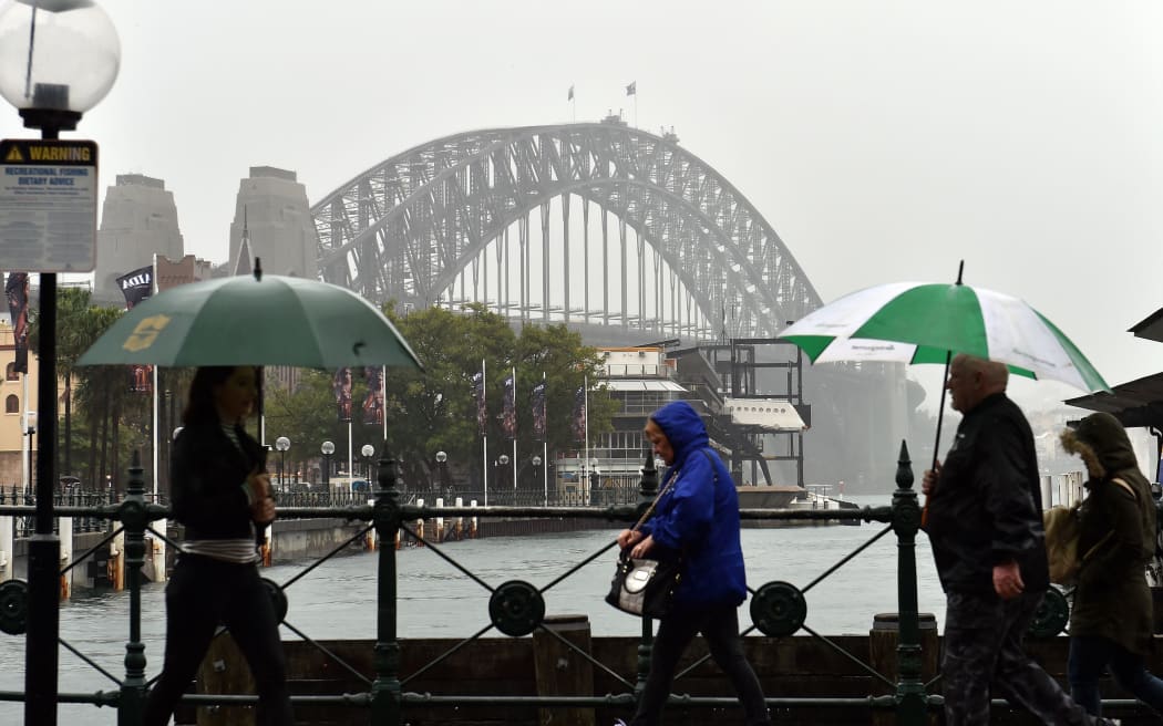 Commuters make their way in the heavy rain in front of the Sydney Habour Bridge.