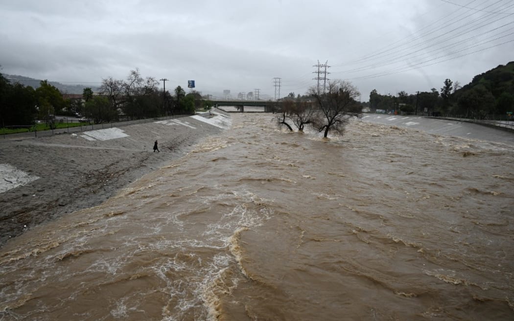 A person walks to the edge of the raging Los Angeles River as the second and more powerful of two atmospheric river storms inundate Los Angeles, California, on February 5, 2024. Swaths of the US state of California were flooded on Monday and hundreds of thousands of people were without power after a dangerous storm brought heavy rains and prompted a state of emergency. (Photo by Robyn Beck / AFP)