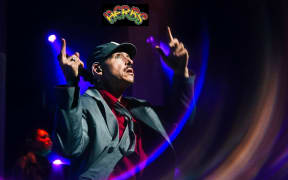 Tom Scott raises his forefingers in the air where the logo for the band Herbs has been placed.