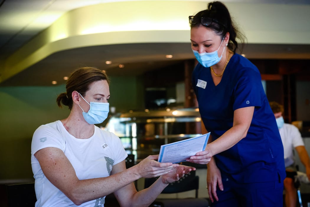 Three time Olympian Australian swimmer Cate Campbell (L) receives a fact sheet  on 10 May 2021, upon receiving the Pfizer/BioNTech vaccination against Covid-19 after the Australian Olympic Committee began their rollout of vaccinations for members of the Olympic team ahead of the the games in Tokyo.