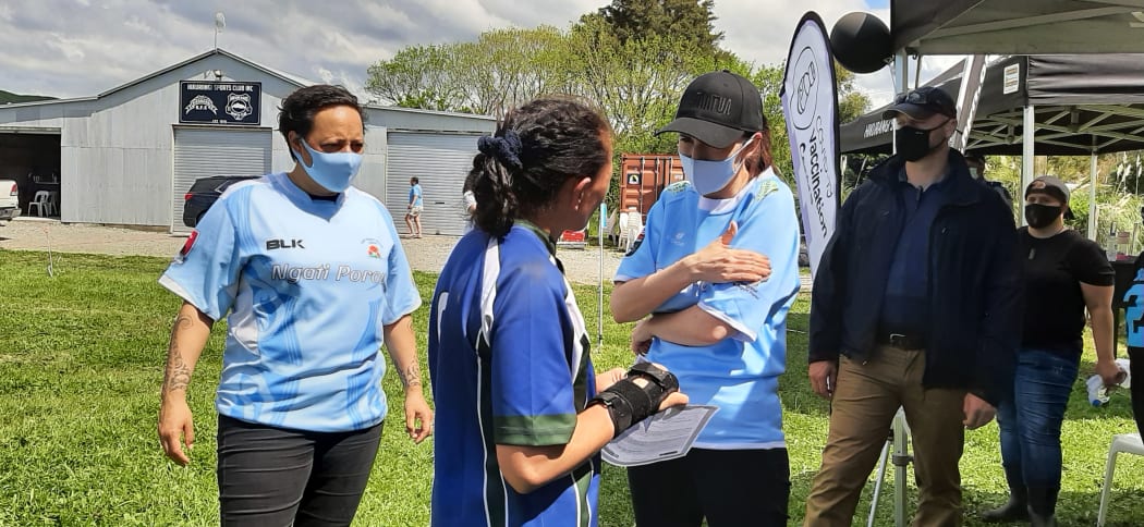 Prime Minister Jacinda Ardern, flanked by East Coast MP Kiri Allan, describes what the vaccine needle feels like to one of the rugby players at today’s game in Ruatōrea.