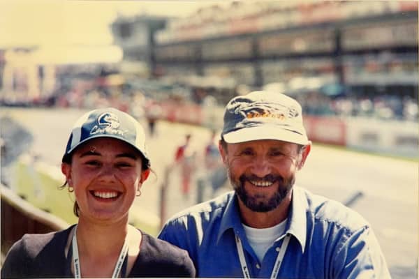 A smiling young woman and midlife man wear caps in the sunshine.