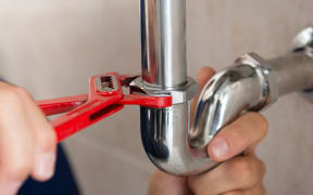 A plumber fixes a pipe with a wrench.