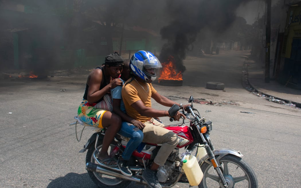 A woman with a child lowers her head as they leave the area on a motorcycle after gunshots were heard in Port-au-Prince, Haiti, on 20 March, 2024. Negotiations to form a transitional council to govern Haiti advanced on March 20, as the United States airlifted more citizens to safety from gang violence that has plunged the impoverished country into chaos. (Photo by Clarens SIFFROY / AFP)
