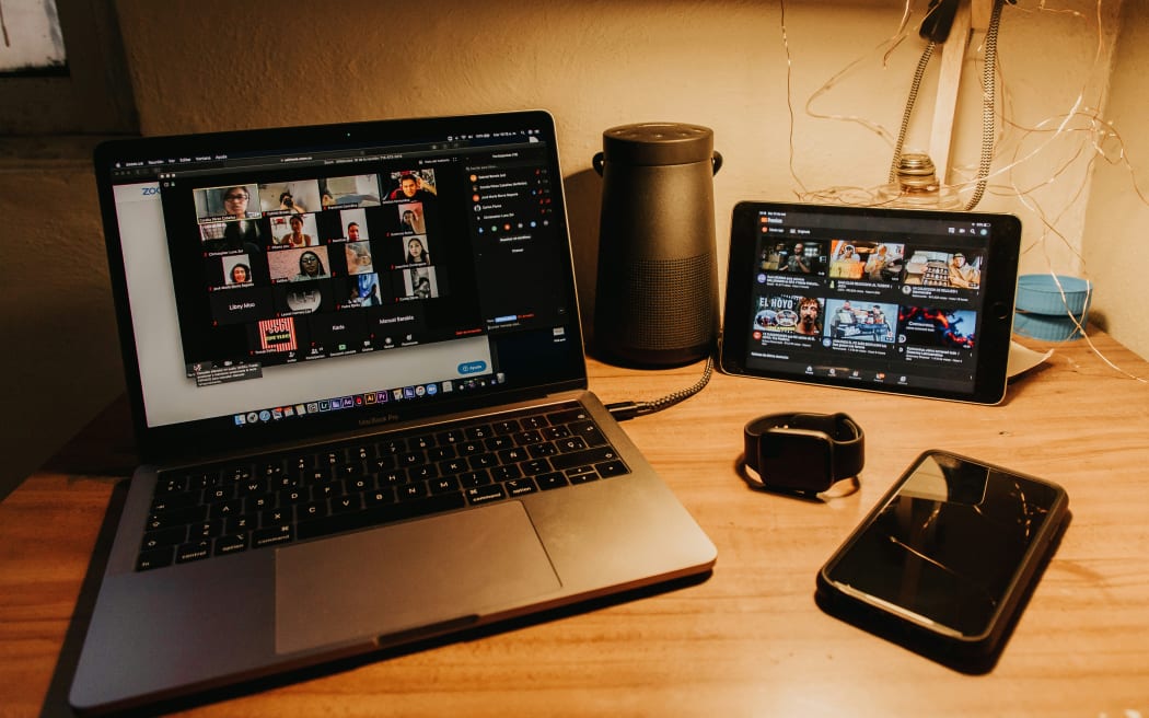 A laptop, tablet and mobile phone on a wooden table illustrating video calling.