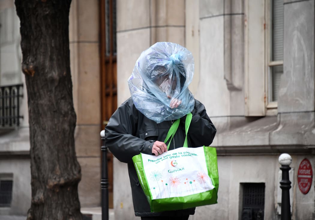 As anxiety increases, a man protects his face with a plastic bag as he walks in the street in Paris.