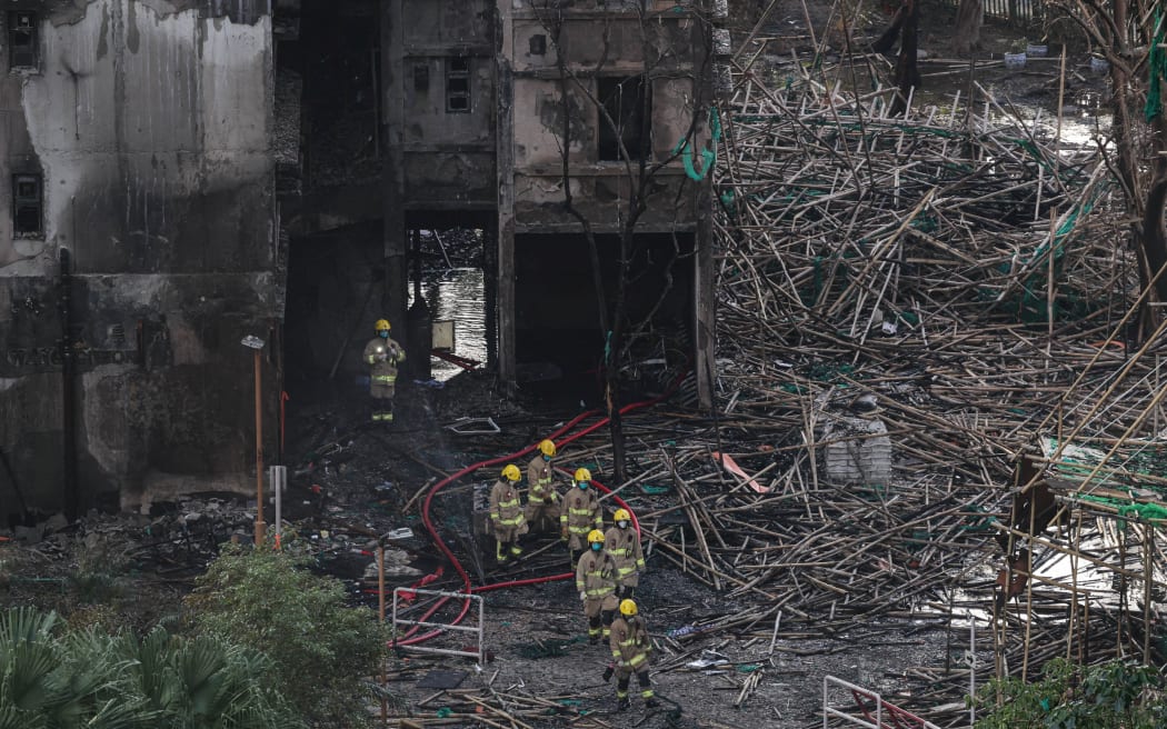 Firefighters walk through charred bamboo scaffolding as they exit a fire-damaged residential block at Wang Fuk Court housing complex, following a deadly fire on Wednesday, in Tai Po, Hong Kong, on November 29, 2025.