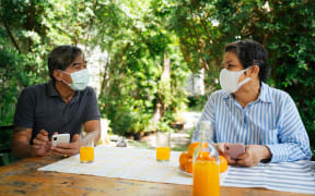 Couple wearing masks picnicking outdoors.