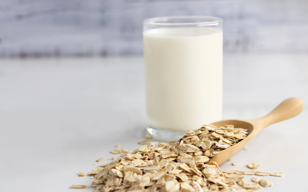 A glass of milk and oats in spoon.