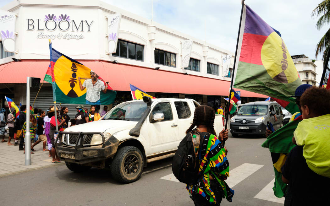 A pick-up carries a kanak flag bearing the image of independantist leader Eloi Machoro killed in 1985 in a law enforcement operation, during a demonstration against the enlargement of the electorate for the forthcoming provincial elections in New Caledonia, in Noumea, on April 13, 2024. Nearly 32,000 independents (15,000) and non-independents (17,000) gather on April 13, 2024, according to the police, for the expansion of the electorate for the upcoming provincial elections in New Caledonia. The constitutional bill to open the electorate to people who have been resident in the territory for at least ten years is currently before Parliament and has reignited tensions between supporters of independence and its opponents. (Photo by Theo Rouby / AFP)