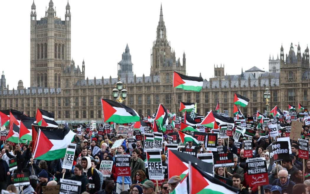 Protesters hold placards and wave Palestinian flags as they walk over Westminster Bridge with the Palace of Westminster, home of the Houses of Parliament behind during a 'March For Palestine' in London on October 28, 2023, to call for a ceasefire in the conflict between Israel and Hamas. Thousands of civilians, both Palestinians and Israelis, have died since October 7, 2023, after Palestinian Hamas militants based in the Gaza Strip entered southern Israel in an unprecedented attack triggering a war declared by Israel on Hamas with retaliatory bombings on Gaza. (Photo by HENRY NICHOLLS / AFP)