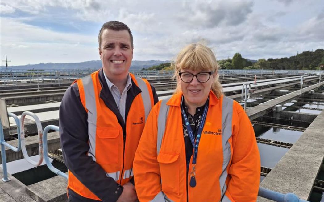 A picture of two people in high-vis shirts, smiling in front of the Ardmore Water Treatment Plant.