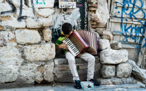A Young street musicians plays the piano accordion on a street in the Plaka district of Athens.